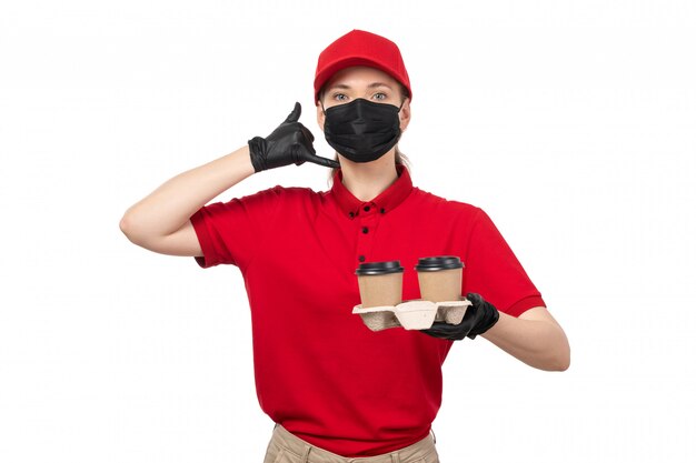 Widok z przodu żeński kurier w czerwonej koszuli, czerwonej czapce, czarnych rękawiczkach i czarnej masce, trzyma kawę z prośbą o wezwanie pozowanie na biały