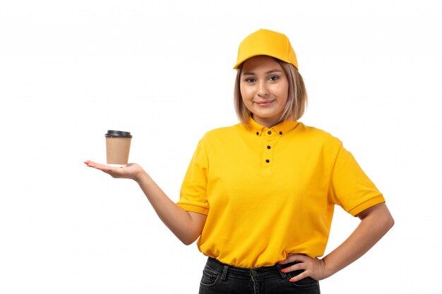 Widok z przodu żeński kurier w żółtej koszuli, żółtej czapce i czarnych dżinsach, uśmiechnięty, trzymając filiżankę kawy na białym tle