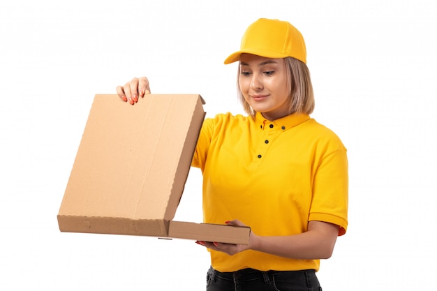 Widok z przodu żeński kurier w żółtej koszuli, żółtej czapce i czarnych dżinsach, uśmiechnięty, trzymając pudełko po pizzy otwierające je na białym tle