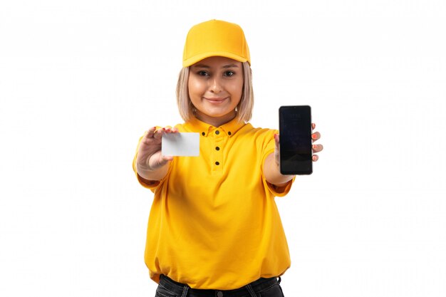 Widok z przodu żeński kurier w żółtej koszuli, żółtej czapce, trzymając smartfon i białą kartę, uśmiechając się na białym tle