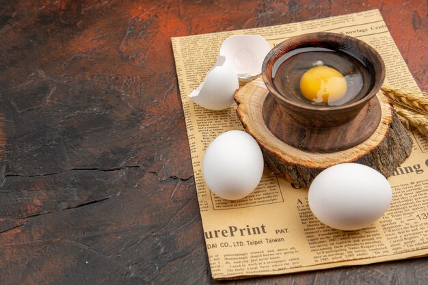 Widok z przodu złamane surowe jajko wewnątrz talerza z innymi jajkami na ciemnej powierzchni