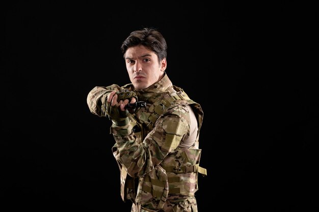 Bezpłatne zdjęcie widok z przodu żołnierza wojskowego w mundurze trzymającego pistolet na czarnej ścianie
