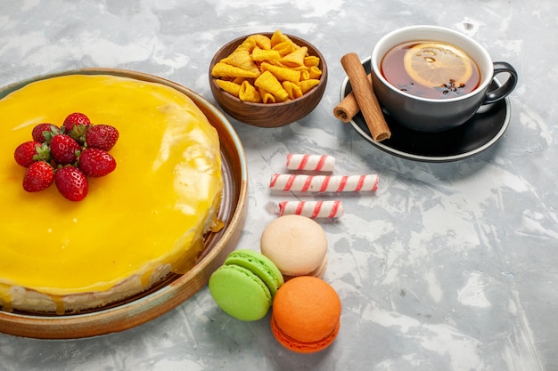 Widok z przodu żółte ciasto z makaronikami i filiżanką herbaty na białej powierzchni