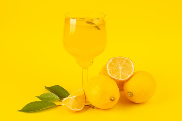 Widok z przodu żółte świeże cytryny świeże dojrzałe w całości i pokrojone w plasterki cytrynowy napój wewnątrz szklanych owoców odizolowanych na żółtym tle kolor owoców cytrusowych