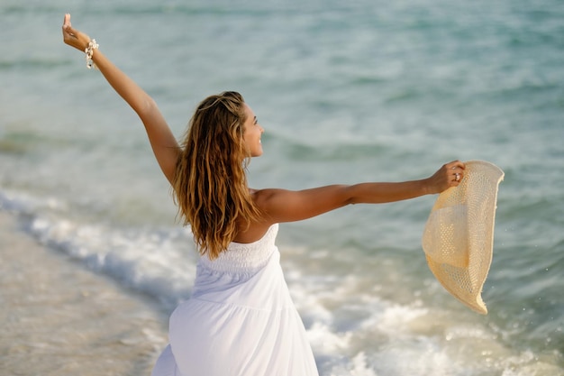 Bezpłatne zdjęcie widok z tyłu figlarnej kobiety cieszącej się letnim dniem, stojąc na brzegu z rozpostartymi ramionami