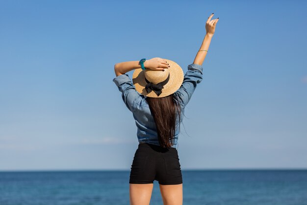 Widok z tyłu. kobieta w słomkowym kapeluszu, z postacią patrząc na morze.