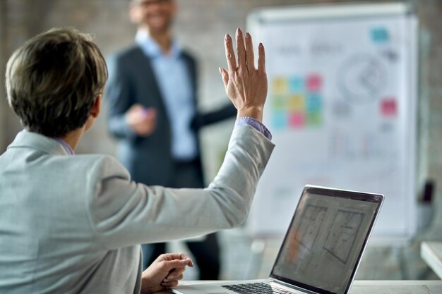Widok z tyłu kobiety przedsiębiorcy podnoszącej rękę, aby odpowiedzieć na pytanie podczas prezentacji biznesowej w biurze