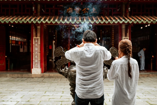 Widok z tyłu mężczyzny i kobiety modlących się w świątyni z płonącym kadzidłem