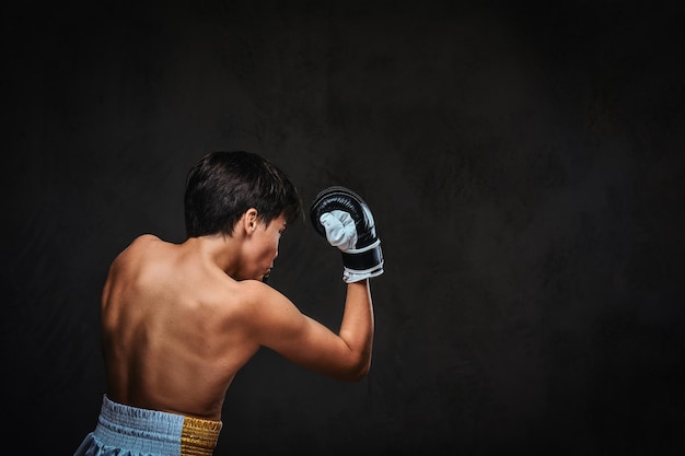 Widok z tyłu młodego boksera bez koszuli podczas ćwiczeń bokserskich, skoncentrowany na procesie z poważną skoncentrowaną twarzą.