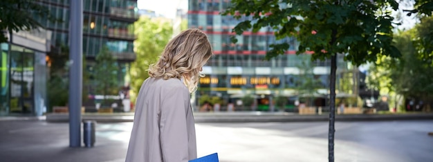 Bezpłatne zdjęcie widok z tyłu młodej kobiety w garniturze spacerującej ulicą, trzymającej teczkę z dokumentami jadącymi do pracy lub dalej