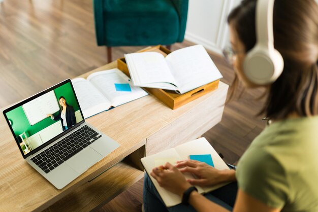 Widok z tyłu młodej studentki zwracającej uwagę i słuchającej nauczyciela online na laptopie w domu