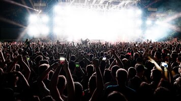Bezpłatne zdjęcie widok z tyłu podekscytowanej publiczności z podniesionymi rękami wiwatującymi przed sceną na koncercie muzycznym