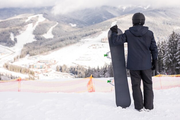 Widok z tyłu sportowca ze snowboardem oglądającym tor jazdy