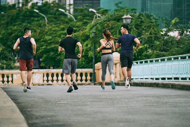 Widok z tyłu trzech mężczyzn i dziewczyny jogging razem w letni dzień