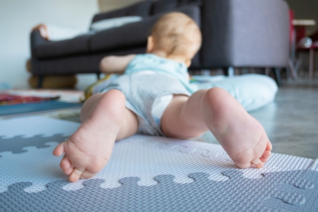 Widok zbliżenie nogi lub stopy małego dziecka. Śliczne urocze niemowlę leżące na brzuchu i bawiące się na miękkiej podłodze w domu. Koncepcja dzieciństwa i niemowlęctwa