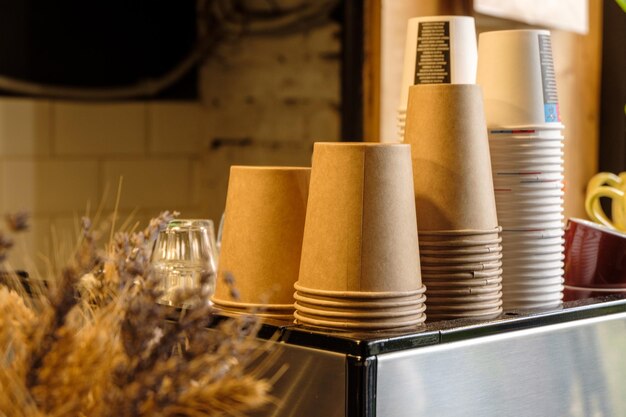 Wiele papierowych kubków wielokrotnego użytku w lokalnej kawiarni na ekspresie do kawy w pobliżu niektórych kwiatów ozdobnych