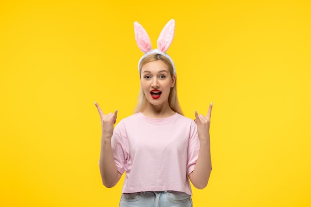 Bezpłatne zdjęcie wielkanoc piękna śliczna blondynka z uszami królika uśmiecha się i pokazuje znak rocka