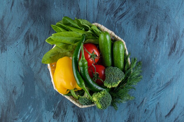 Wiklinowa miska świeżych organicznych warzyw na niebieskiej powierzchni. .