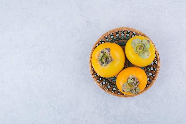 Wiklinowa Miska Trzech Persimmons Na Białym Tle. Zdjęcie Wysokiej Jakości