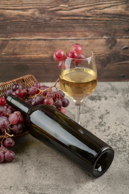 Bezpłatne zdjęcie wiklinowy kosz czerwonych winogron z lampką białego wina na marmurowym stole.