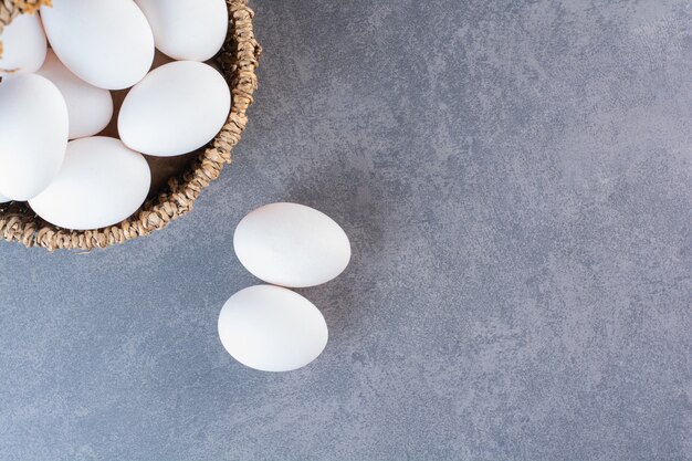 Wiklinowy kosz pełen ekologicznych jajek na kamiennym stole.