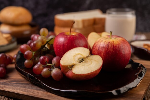 Winogrona, jabłka i chleb w talerzu na stole