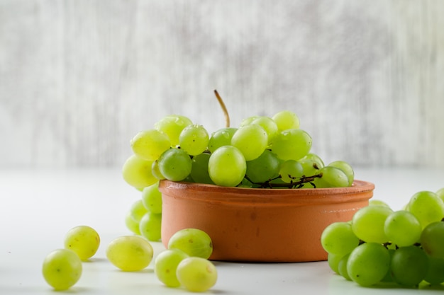 Bezpłatne zdjęcie winogrona w glinianym talerzu na biel powierzchni, boczny widok.