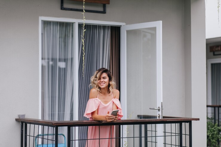 Bezpłatny plik Zdjęcie winsome opalona dziewczyna z telefonem w ręce, uśmiechając się i odwracając wzrok. wesoła młoda dama w różowym stroju stojącym na balkonie hotelu.