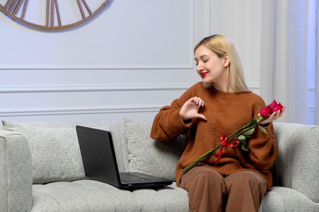 Wirtualna miłość ładna młoda blondynka w przytulnym swetrze na komputerową randkę na odległość pokazującą znak miłości