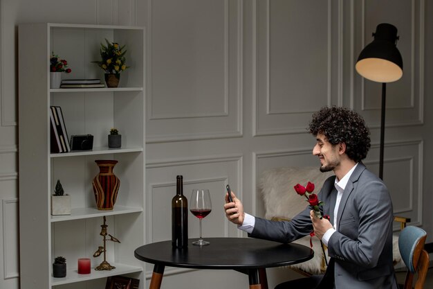 Wirtualna miłość przystojny ładny facet w garniturze z winem na randkę na odległość trzymającą kwiaty