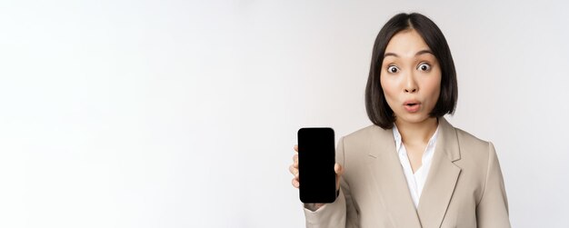 Wizerunek Azjatyckiej Kobiety Korporacyjnej Pokazującej Interfejs Aplikacji Ekran Telefonu Komórkowego Robiący Zdziwioną Twarz Wyraz Wow Stojący Na Białym Tle