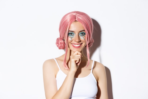 Bezpłatne zdjęcie wizerunek inteligentnej atrakcyjnej dziewczyny z różową peruką i jasnym makijażem, wyglądającej na zadowoloną i uśmiechniętą, mam pomysł, stojącą.