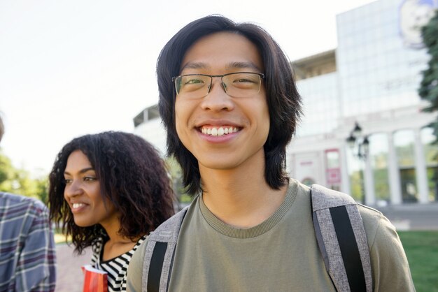 Wizerunek młody rozochocony studencki azjatykci mężczyzna stoi outdoors. Aparat szuka.