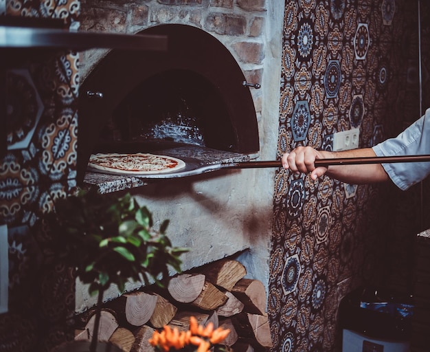 Włoski szef kuchni wkłada świeżo upieczoną pizzę dla smakoszy do kamiennego pieca.