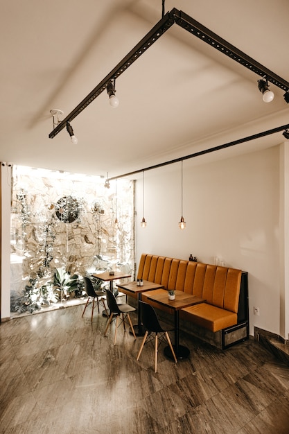 Wnętrze kawiarni z pomarańczową kanapą, trzema stolikami i trzema czarnymi krzesłami