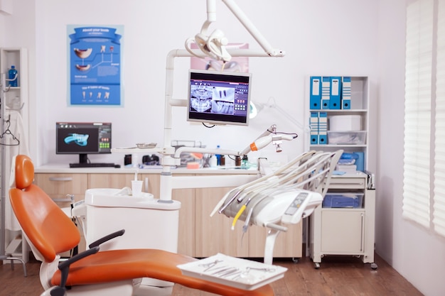 Wnętrze kliniki dentystycznej z nowoczesnym sprzętem stomatologicznym w kolorze pomarańczowym. Gabinet stomatologiczny, w którym nikogo nie ma i pomarańczowy sprzęt do leczenia jamy ustnej.