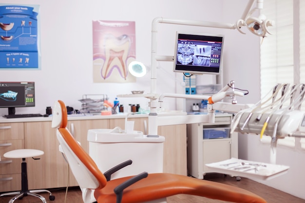 Wnętrze nowoczesnego gabinetu dentystycznego i fotela lekarskiego. Gabinet stomatologiczny, w którym nikogo nie ma i pomarańczowy sprzęt do leczenia jamy ustnej.