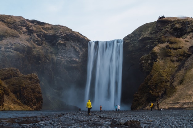 Bezpłatne zdjęcie wodospad skogafoss otoczony ludźmi i skałami pod zachmurzonym niebem na islandii