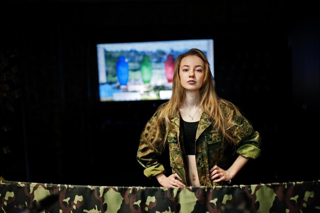 Wojskowa dziewczyna w mundurze kamuflażu na tle armii na strzelnicy