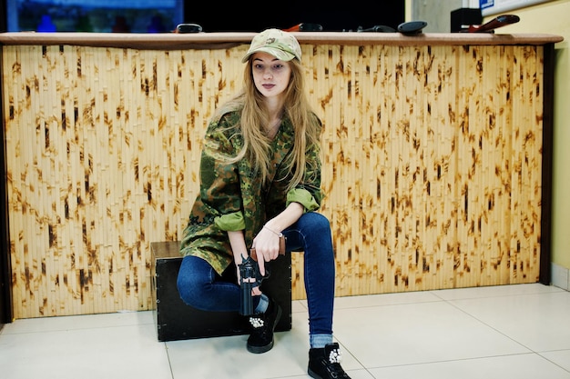 Bezpłatne zdjęcie wojskowa dziewczyna w mundurze kamuflażu z rewolwerem pod ręką na tle armii na strzelnicy