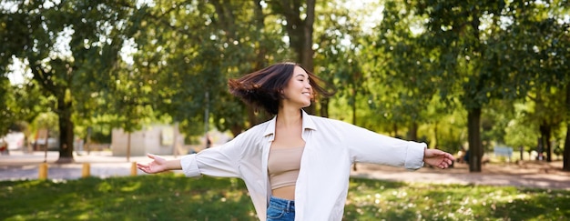 Bezpłatne zdjęcie wolność i koncepcja ludzi szczęśliwa młoda azjatka tańczy w parku wokół drzew uśmiechając się i ciesząc