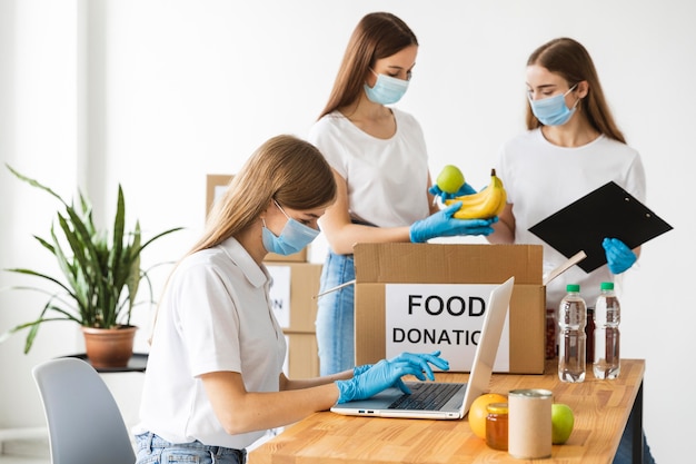 Wolontariusze w rękawiczkach i maskach medycznych przygotowują jedzenie w pudełku do darowizny