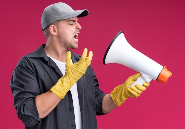 Bezpłatne zdjęcie wściekły młody cholerny facet sprzątający sobie t-shirt i czapkę z rękawiczkami mówi przez głośnik na białym tle na różowej ścianie