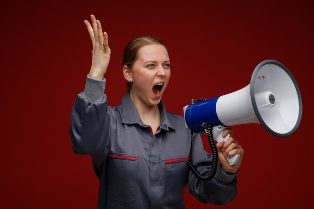 Bezpłatne zdjęcie wściekły młody inżynier blond kobieta ubrana w mundur, patrząc na bok podnosząc rękę krzycząc w głośniku