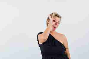 Bezpłatne zdjęcie wspaniała kobieta pokazująca ok gest na oko w czarnej bluzce i wyglądająca na rozbawioną
