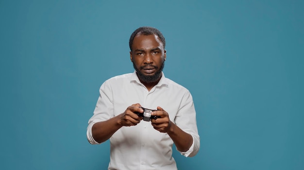 Współczesna osoba używająca kontrolera do grania w gry wideo w studio, bawiąca się rozgrywką online. Tysiącletni mężczyzna gra z joystickiem na konsoli, gra na urządzeniu elektronicznym dla rozrywki.