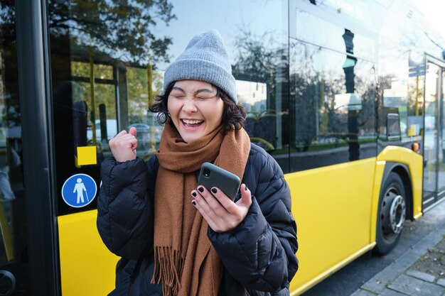 Współcześni ludzie i styl życia szczęśliwa azjatycka dziewczyna krzyczy z radości, świętuje stoiska w pobliżu autobusowego transportu publicznego