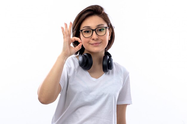 Wwoman w białej koszuli i czarnych słuchawkach robi ok znakowi