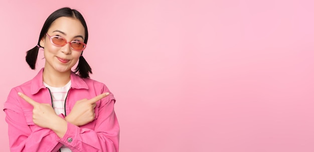 Wybór Stylowa koreańska dziewczyna azjatycka modelka wskazuje palcami na boki, pokazuje dwa warianty reklamy produktu, przedstawiające przedmioty stojące na różowym tle