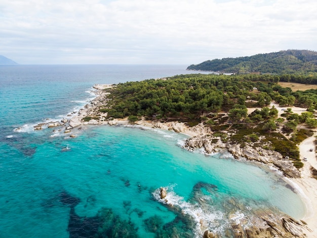 Wybrzeże morza egejskiego z niebieską przezroczystą wodą, zielenią dookoła, skałami, krzewami i drzewami, widok z drona, grecja